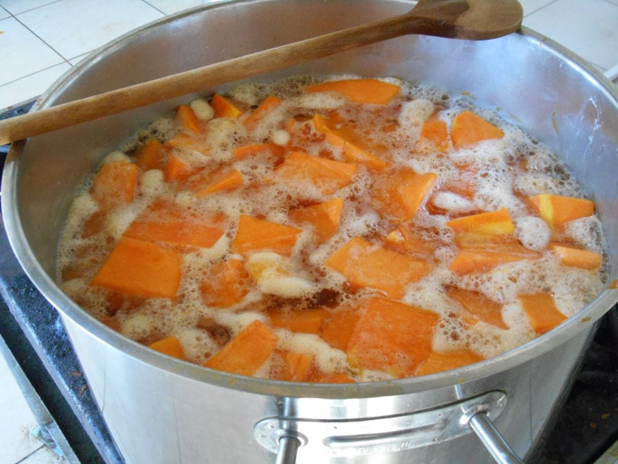pieces of yellow pumpkin boiling in cooking pot and a wooden spoon on top